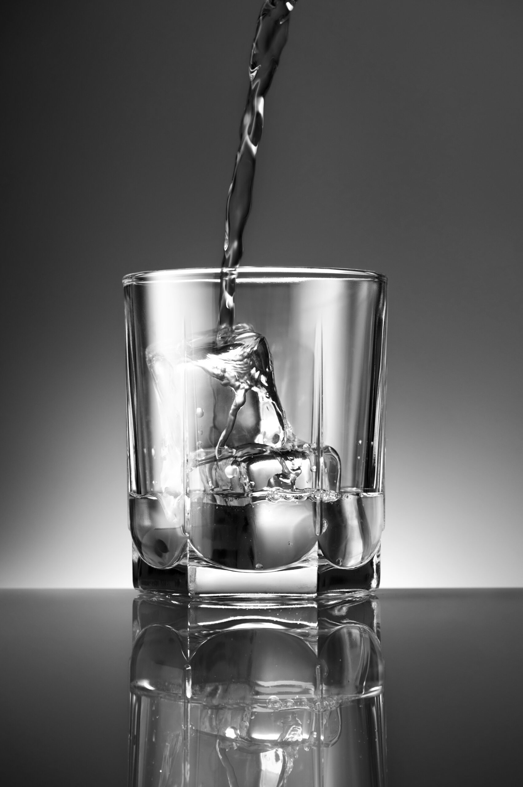 A vertical grayscale shot of pouring a drink into the glass